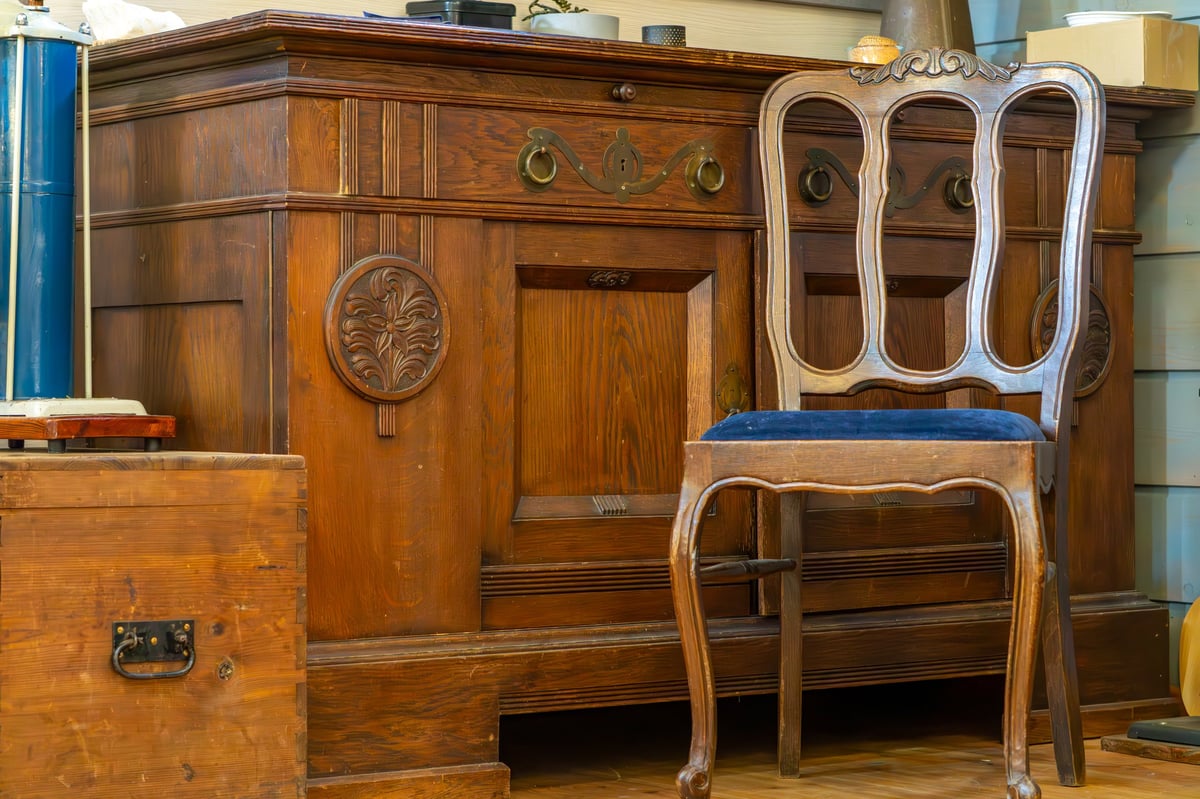 Vintage wooden sideboard with carved details and brass handles, accompanied by an elegant wooden chair featuring a blue upholstered seat
