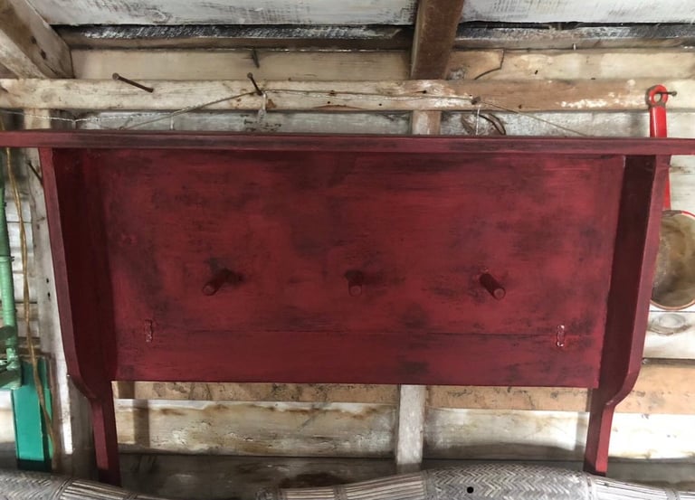 Burgundy velvet upholstered headboard with button tufting against wooden ceiling beams in a workshop setting