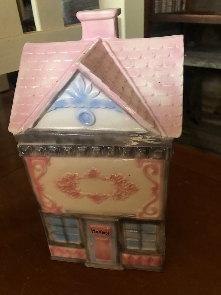 Pink and white toy bakery house with shingled roof, decorative wreath, and storefront windows