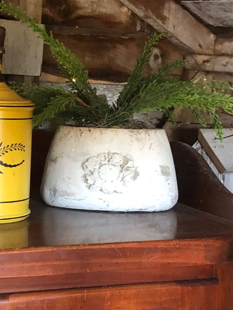 White weathered pot with green succulent plants on wooden shelf next to yellow cylindrical container