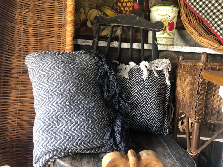 Woven baskets and black and white patterned cushions stored with household items on a shelf