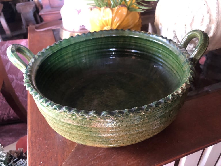 Large green ceramic bowl with textured rim and handles, displayed on a wooden table