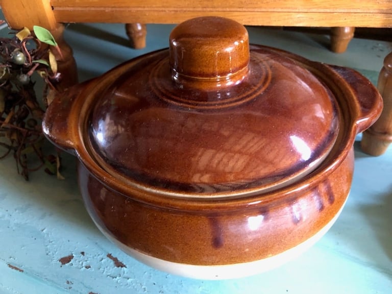 Wooden cooking pot with lid and handles, burnished brown finish, sitting on blue surface with furniture in background