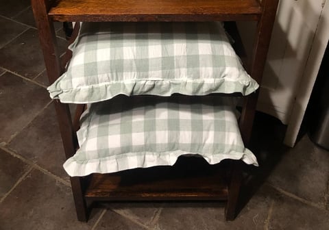 Two stacked pillows with gray and white gingham pattern on a wooden shelf or bench frame