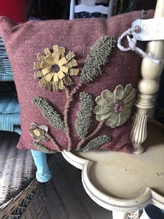 Burgundy cushion cover with embroidered yellow flowers and green stems displayed on a shelf